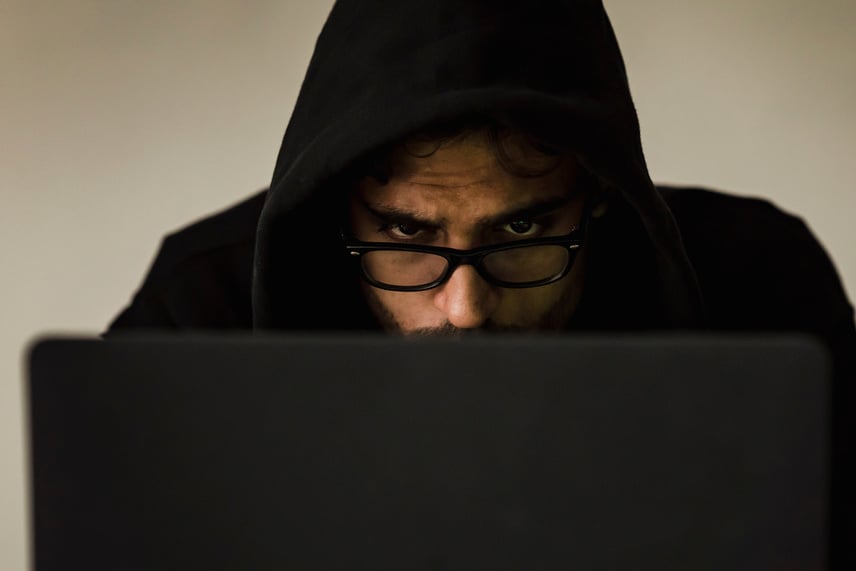 Crop focused hacker in hood using laptop